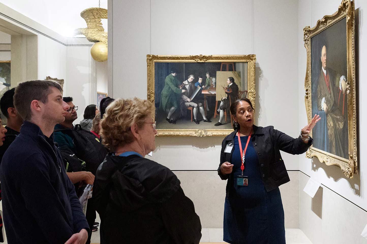 Volunteer gesturing to a portrait of a seated man in front of a crowd